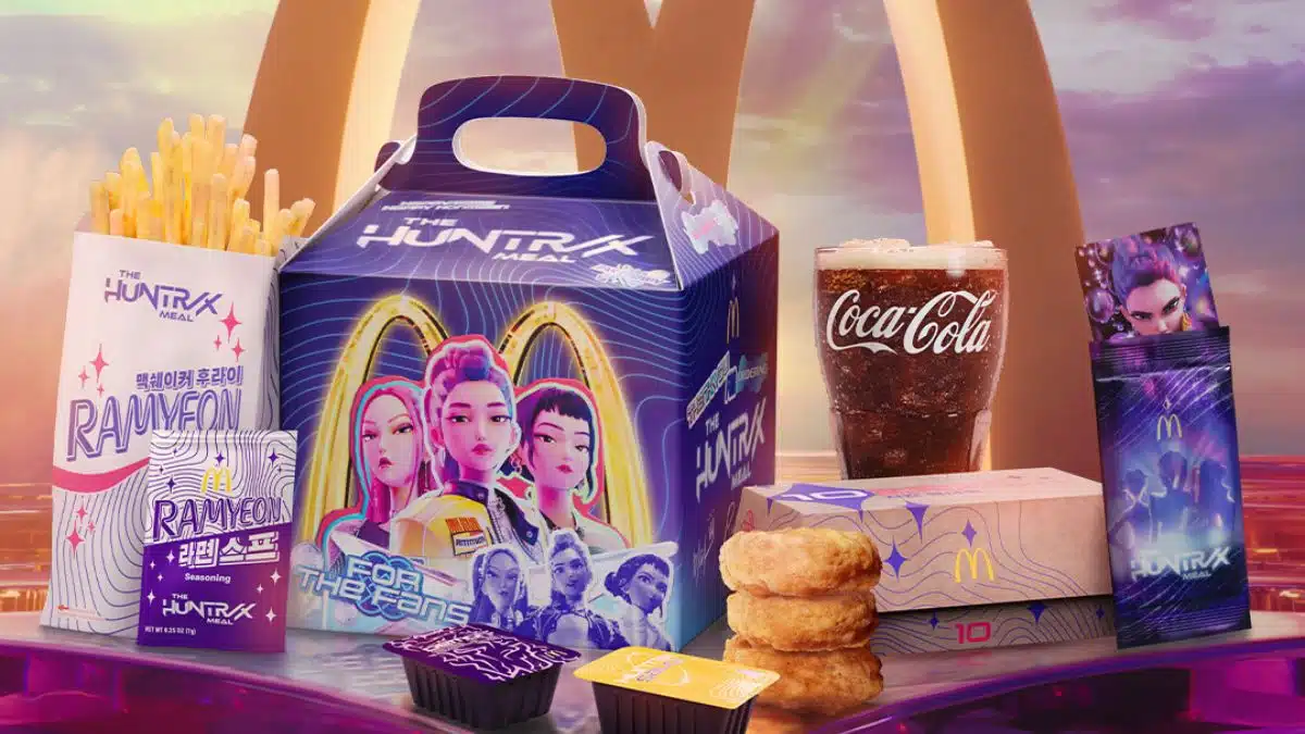 Itens do combo "The Huntress Meal" do McDonald's em colaboração com a Netflix, exibindo uma caixa personalizada com personagens de K-Pop, batatas fritas, nuggets, Coca-Cola e envelopes de tempero em tons de roxo e rosa.