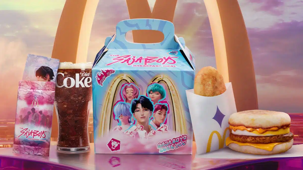 Itens do combo "The SajaBoys Breakfast Meal" do McDonald's, com uma caixa azul clara ilustrada com uma boy band de anime, acompanhada de um McMuffin, hash brown, Diet Coke e cards colecionáveis.