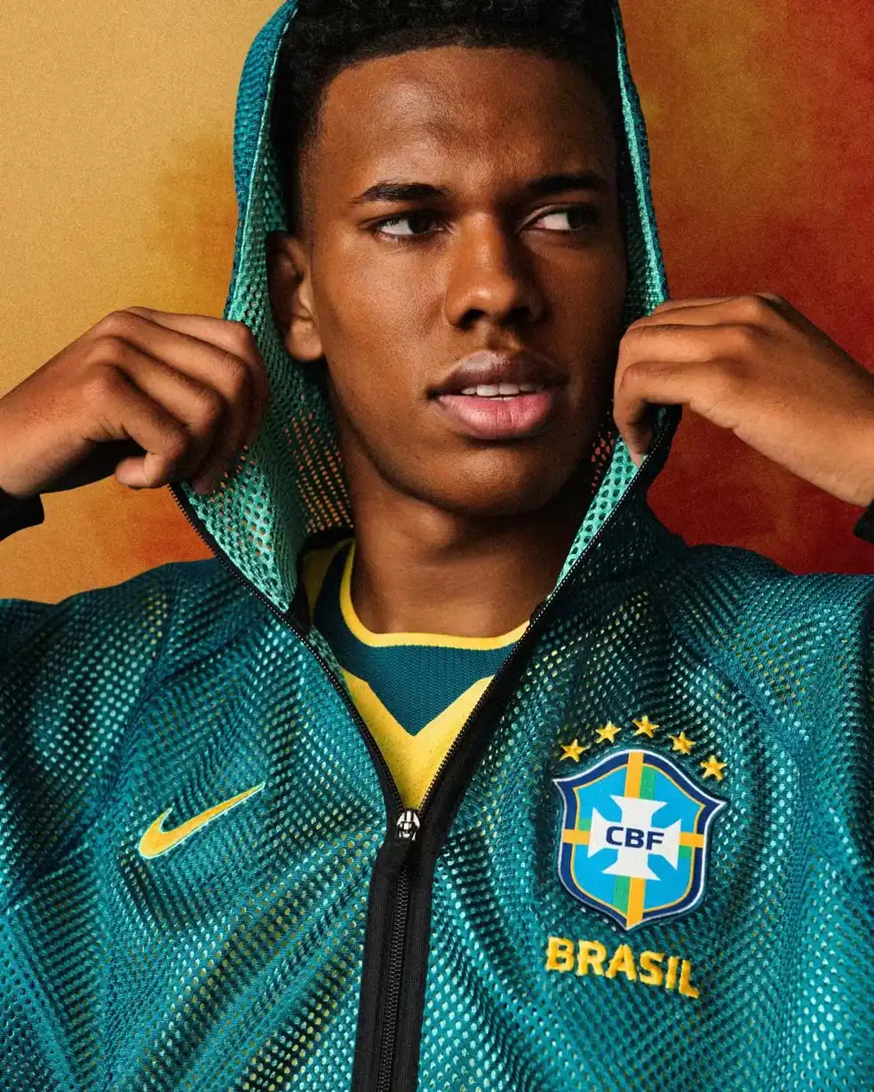 close-up de um homem vestindo um casaco com capuz de malha verde-azulado da seleção brasileira de futebol com o logotipo da CBF.