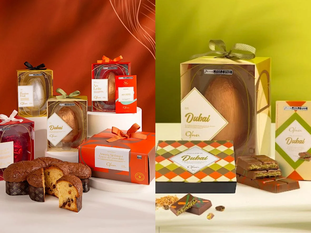 Escultura de chocolate da Ofner composta por um ovo branco salpicado e lascas de chocolate sobre base de musgo, com uma pintura colorida de coelho ao fundo.