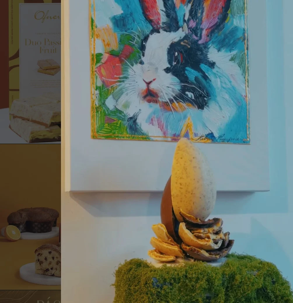 Ovo de Páscoa artesanal da Ofner exposto sobre base de musgo, posicionado em frente a uma tela colorida de um coelho em estilo expressionista.