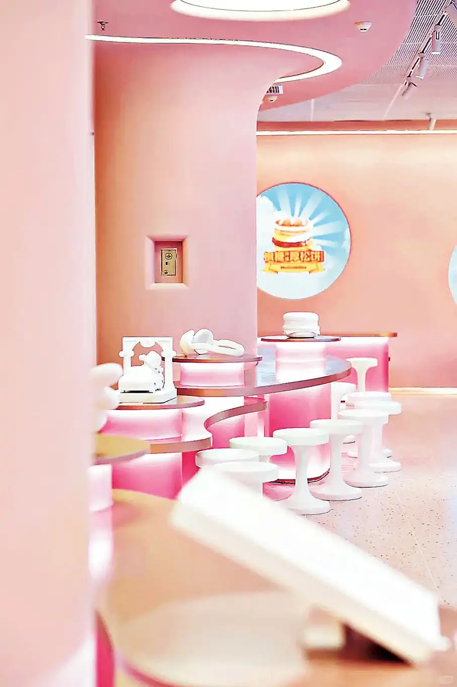 Área de assentos de um restaurante McDonald's temático em tons de rosa, com balcões curvos iluminados, banquetas brancas modernas e janelas circulares.