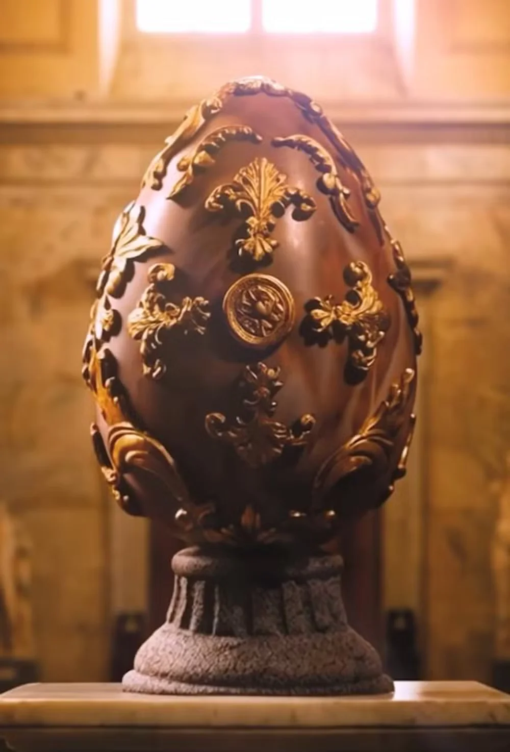 Um close de um ovo decorativo de mármore marrom e preto em um pedestal de pedra com detalhes dourados.