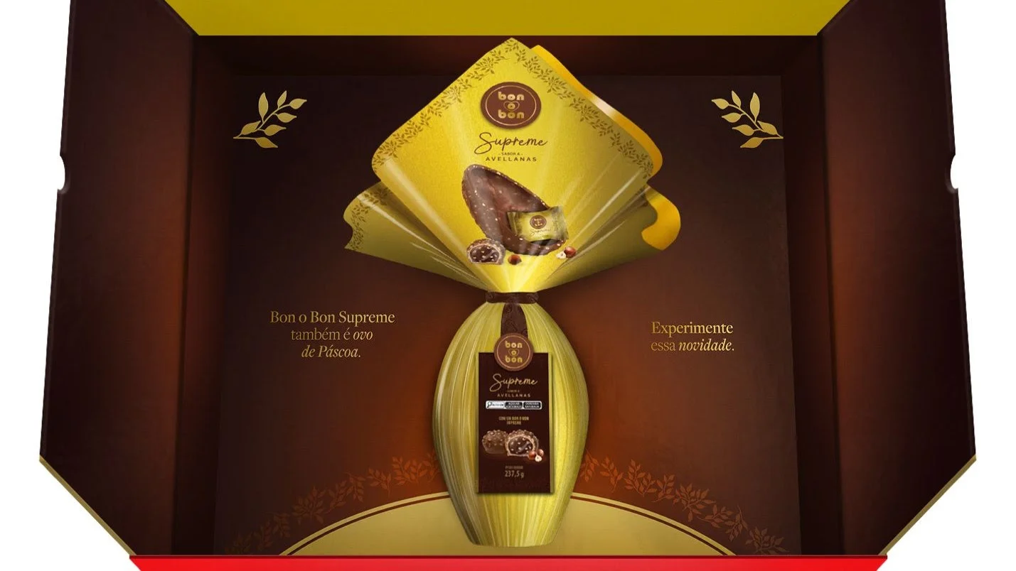 Interior de uma caixa de presente marrom revelando um Ovo de Páscoa Bon o Bon Supreme em embalagem dourada. Ao lado, o texto "Experimente essa novidade".