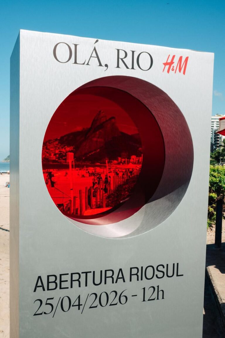 Totem metálico da H&M na Praia de Ipanema com um recorte circular de lente vermelha mostrando o Morro Dois Irmãos.