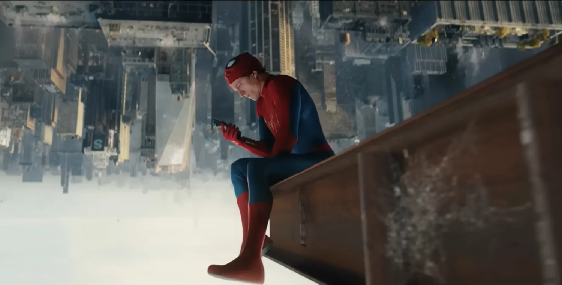 O Homem-Aranha está sentado em uma viga de metal, de ponta-cabeça, olhando para um smartphone. O cenário ao seu redor é de Nova York, com prédios e ruas também invertidos. A imagem é uma referência ao filme "Homem-Aranha: De Volta ao Lar".