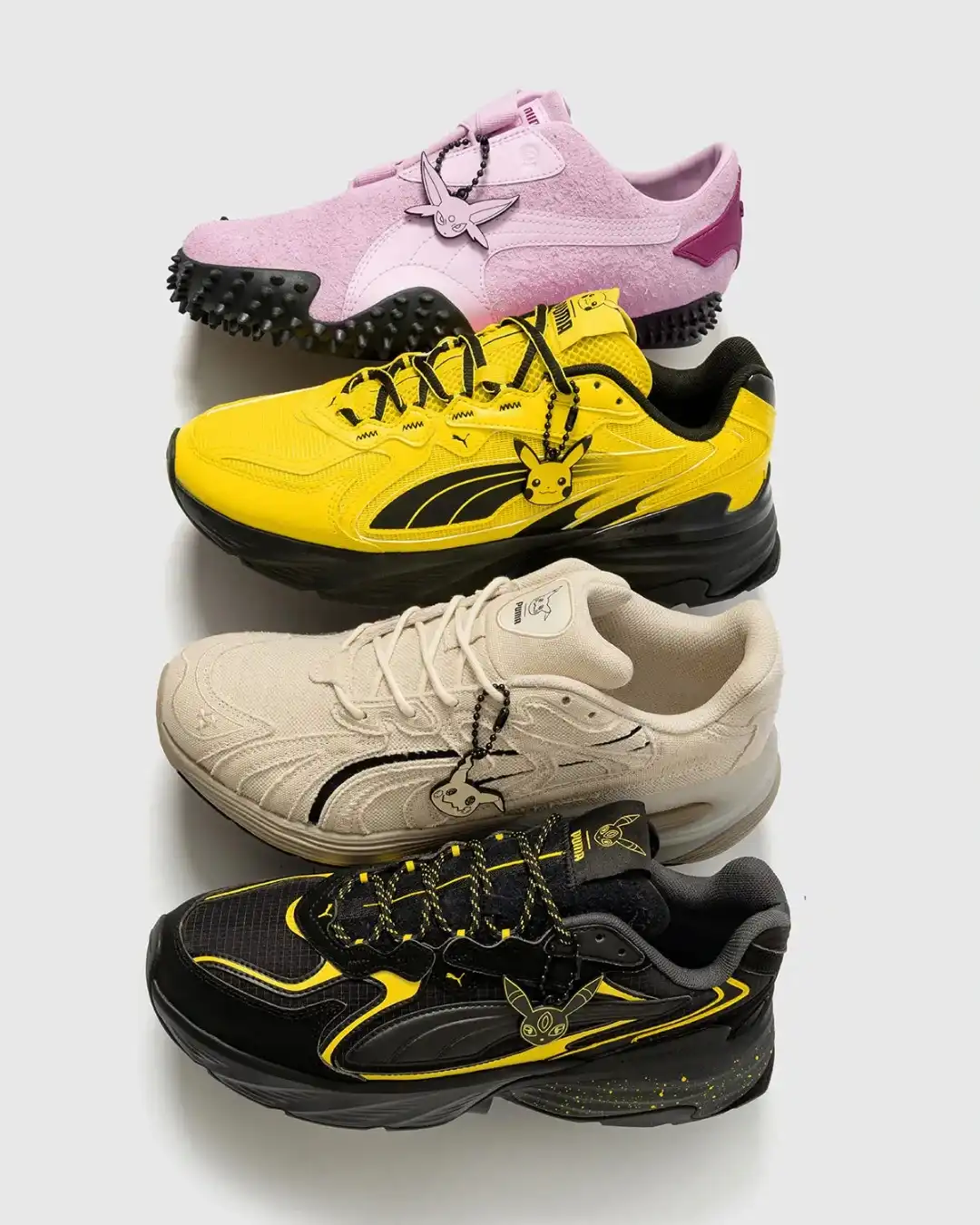 Quatro tênis Puma de cores diferentes empilhados verticalmente, cada um com um pingente de um Pokémon diferente.