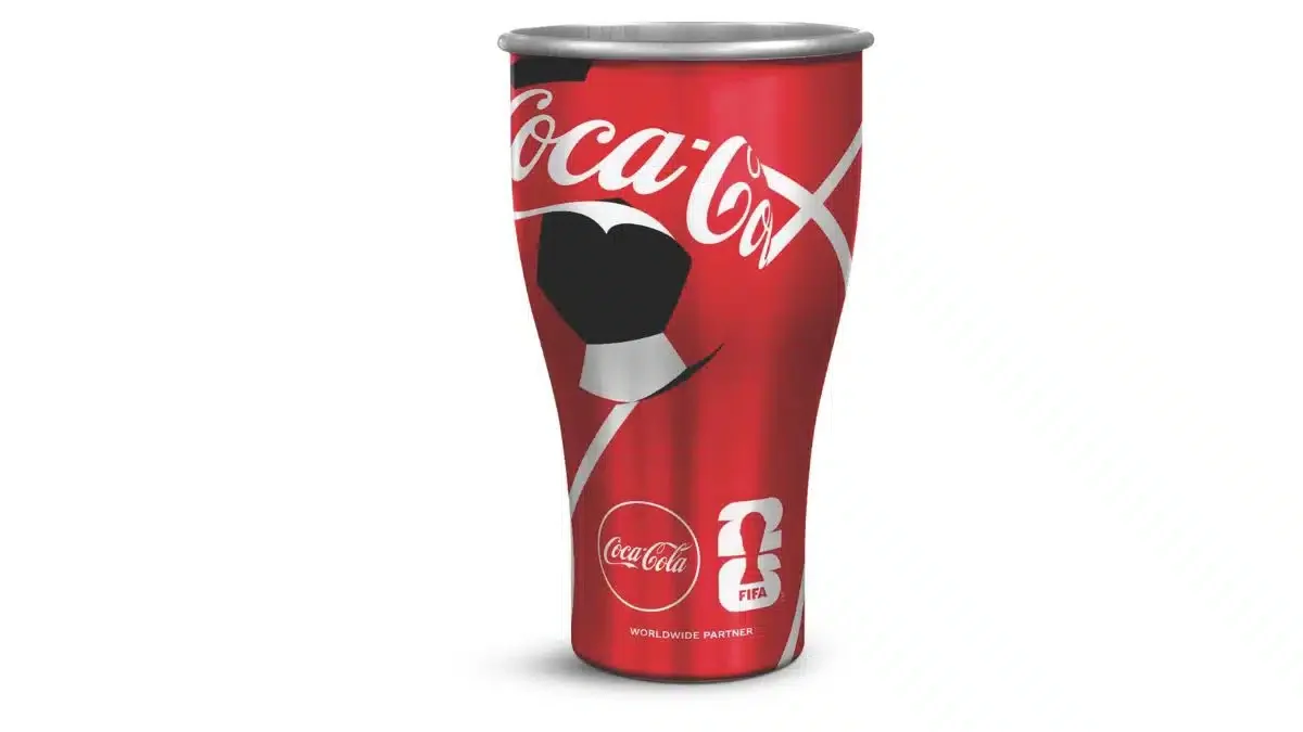 Um copo de metal vermelho da Coca-Cola com tema de futebol isolado em um fundo branco.