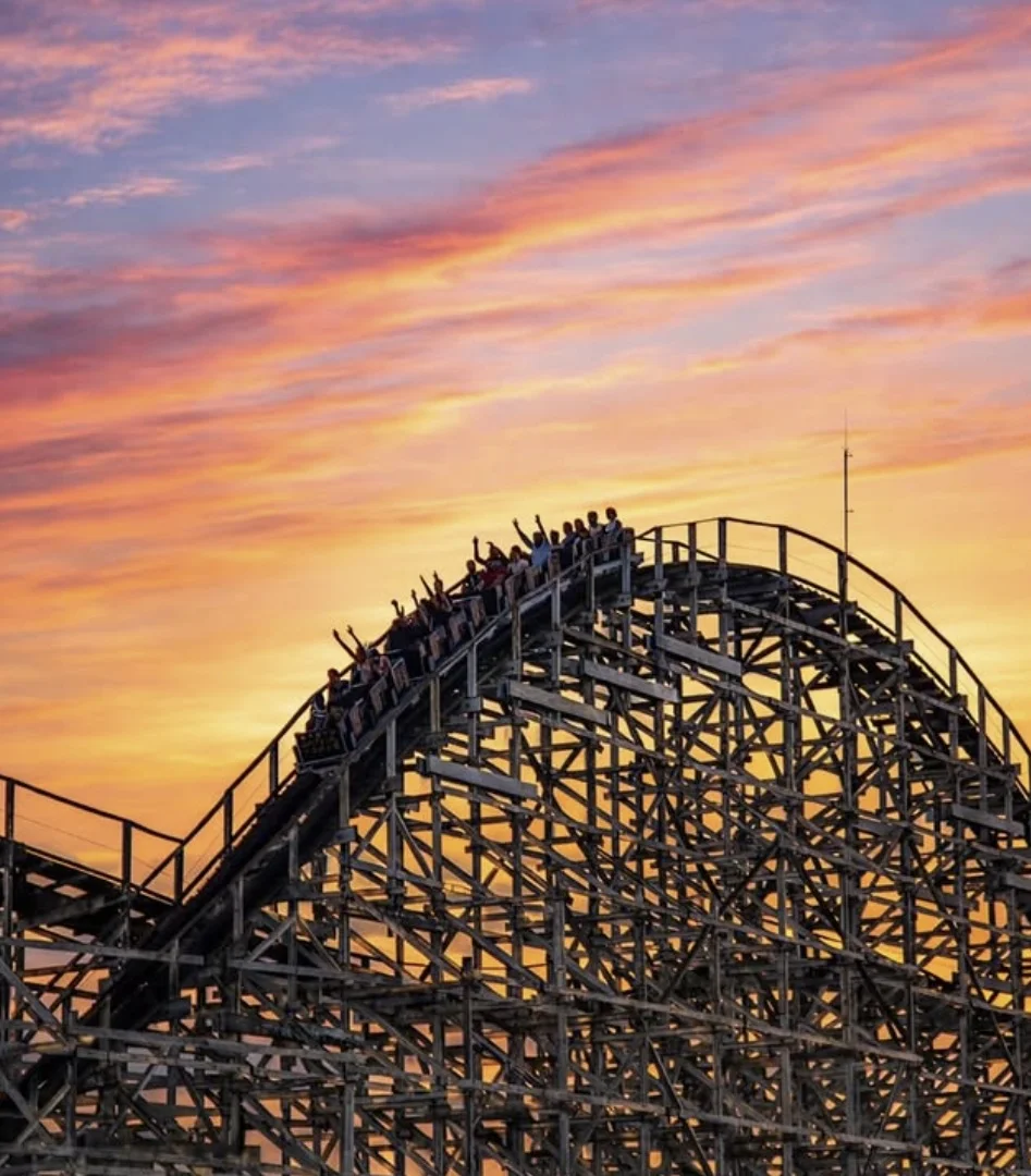 Silhueta da montanha-russa Montezum no Hopi Hari com um carrinho subindo o trilho contra um céu de pôr do sol colorido.