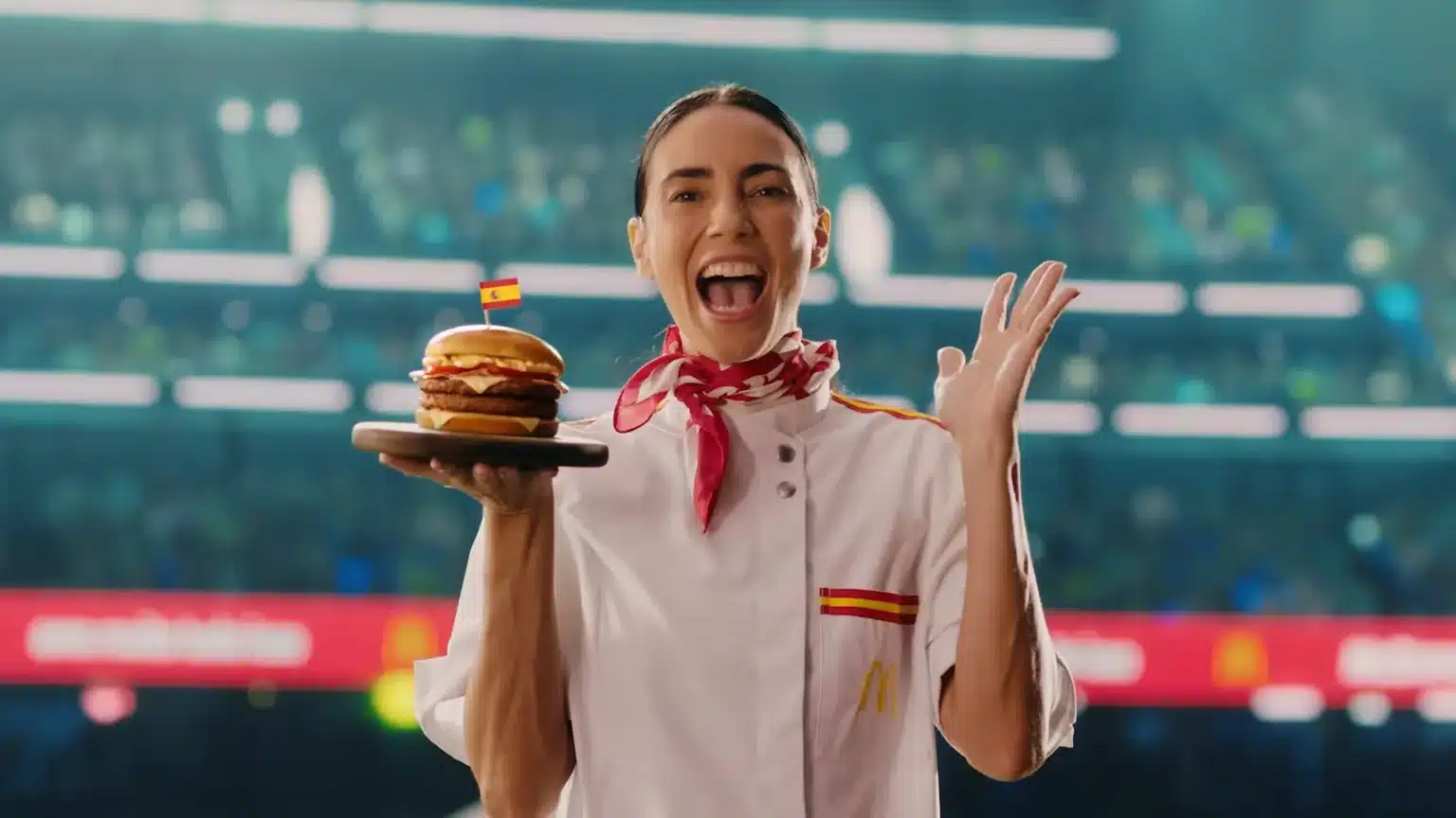 Uma chef de cozinha sorridente em um estádio de futebol, segurando o sanduíche temático da Espanha.
