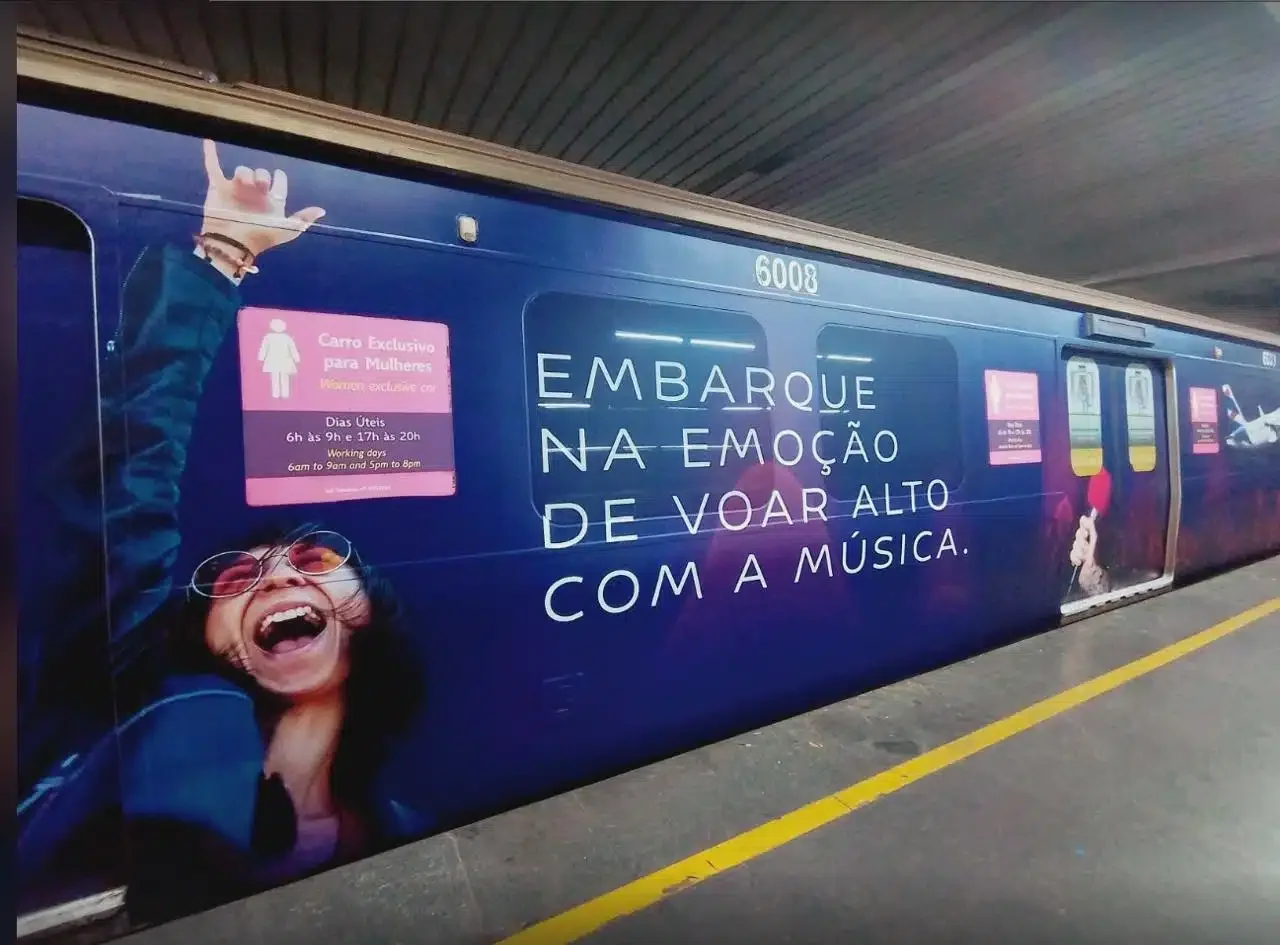 Lateral de um vagão de metrô envelopado com propaganda da LATAM, destacando a frase "Embarque na emoção de voar alto com a música".