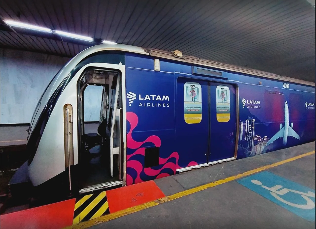 Vista em perspectiva da frente e lateral de um metrô envelopado com a identidade visual da LATAM Airlines.