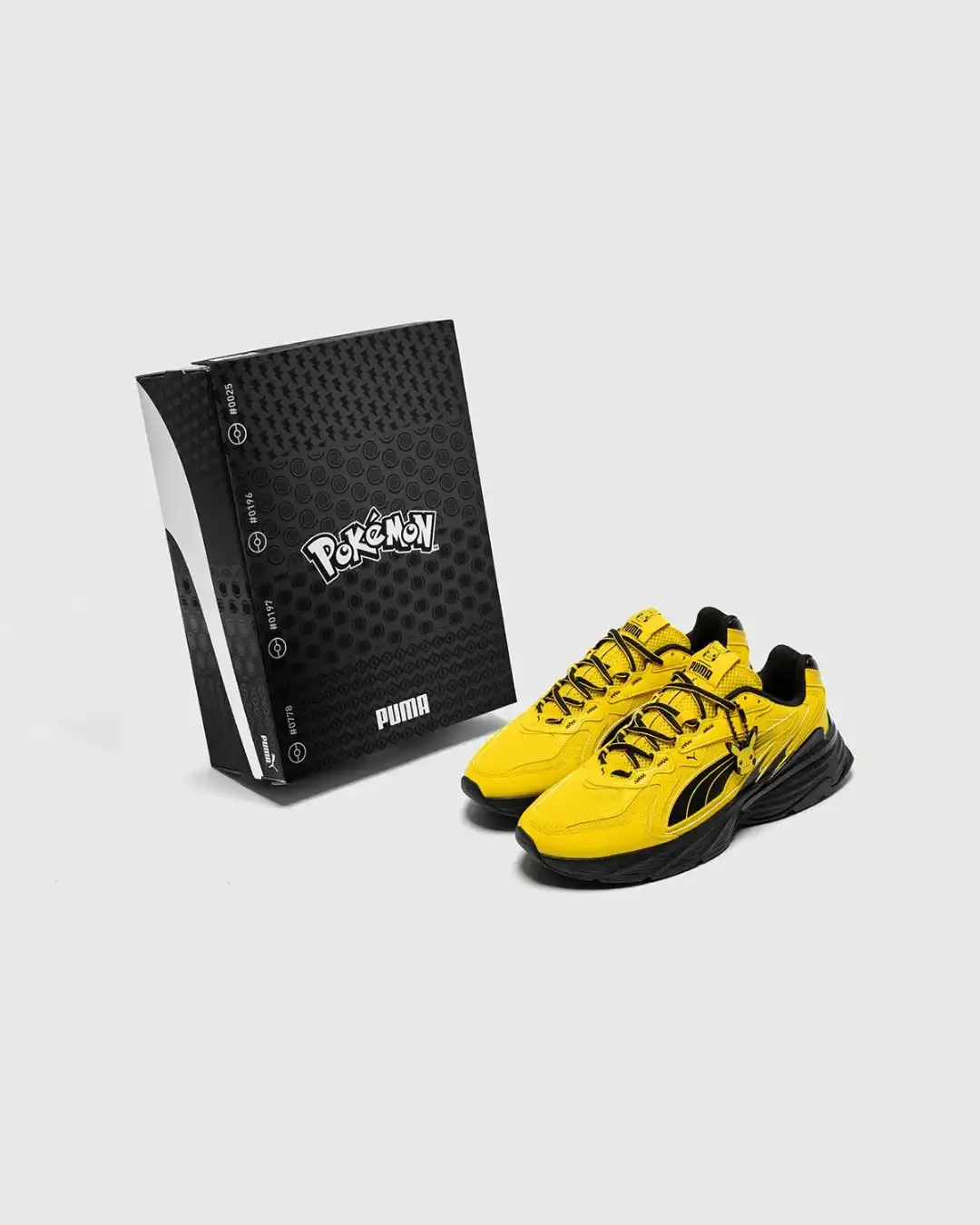 Um par de tênis amarelos do Pikachu ao lado de uma caixa preta estilizada com logotipos da Puma e Pokémon.