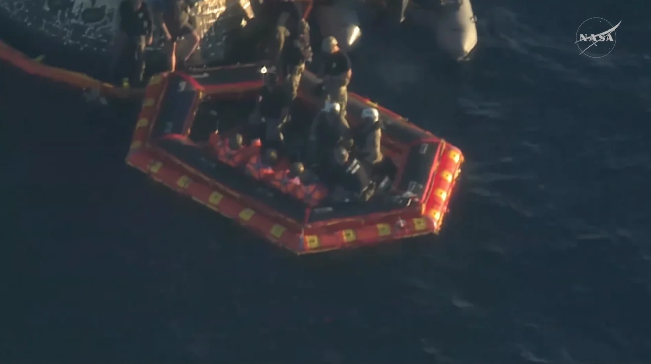 Uma visão de cima para baixo da equipe de recuperação da Marinha dos EUA e dos mergulhadores trabalhando para prender o colar de estabilização inflável laranja brilhante à base da espaçonave Orion no Oceano Pacífico.