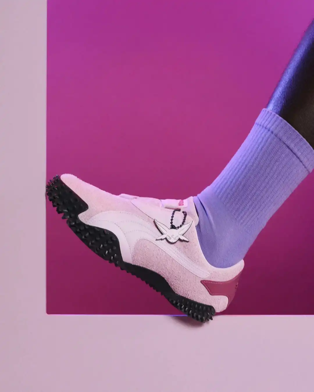 Close lateral de um tênis Puma de camurça rosa com solado tratorado preto, sendo usado com meia lilás.
