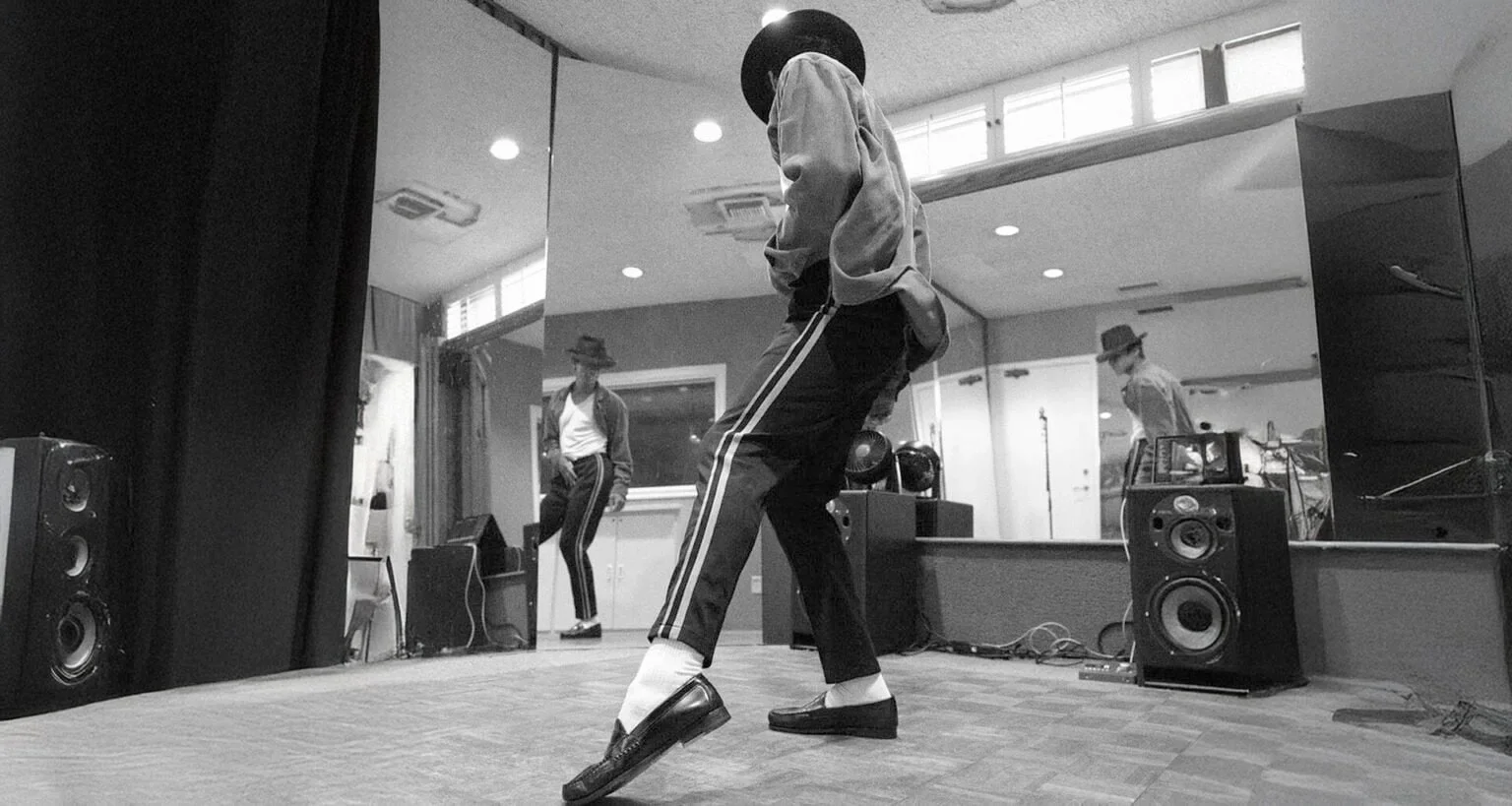 Fotografia em preto e branco de Jaafar Jackson ensaiando passos de dança clássicos de Michael Jackson em frente a um espelho.