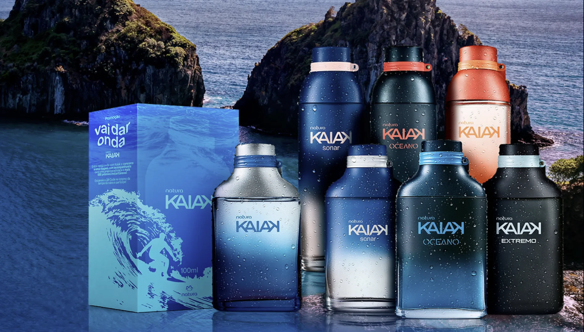 Vários frascos de perfume Natura Kaiak com gotas de água na superfície, posicionados lado a lado. À esquerda, há uma caixa azul com a inscrição "Promoção vai dar onda". Ao fundo, grandes formações rochosas no mar, remetendo a Fernando de Noronha.