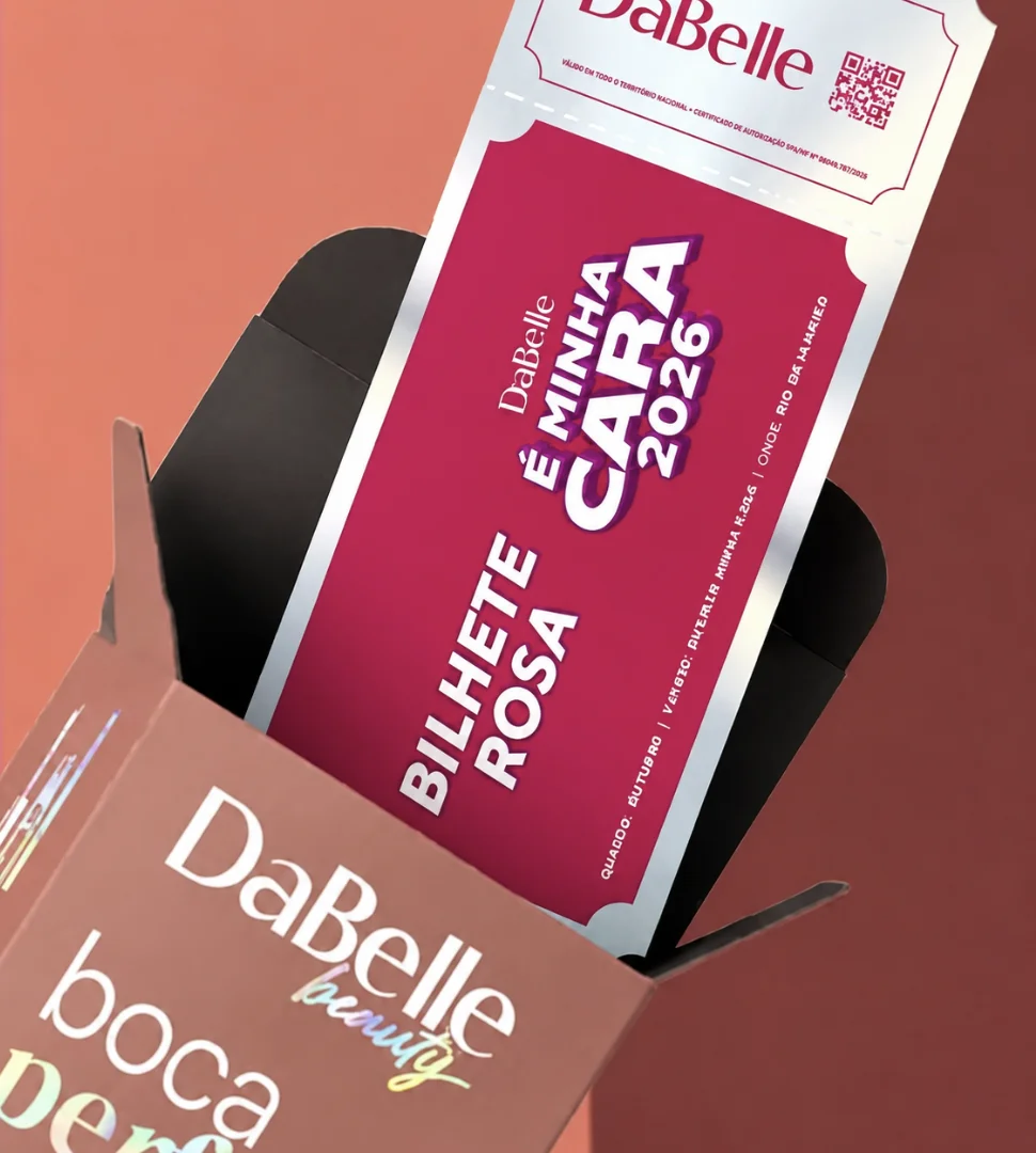 Close em uma embalagem marrom aberta da DaBelle de onde sai um bilhete premiado rosa e metalizado com a inscrição "Bilhete Rosa DaBelle É Minha Cara 2026".