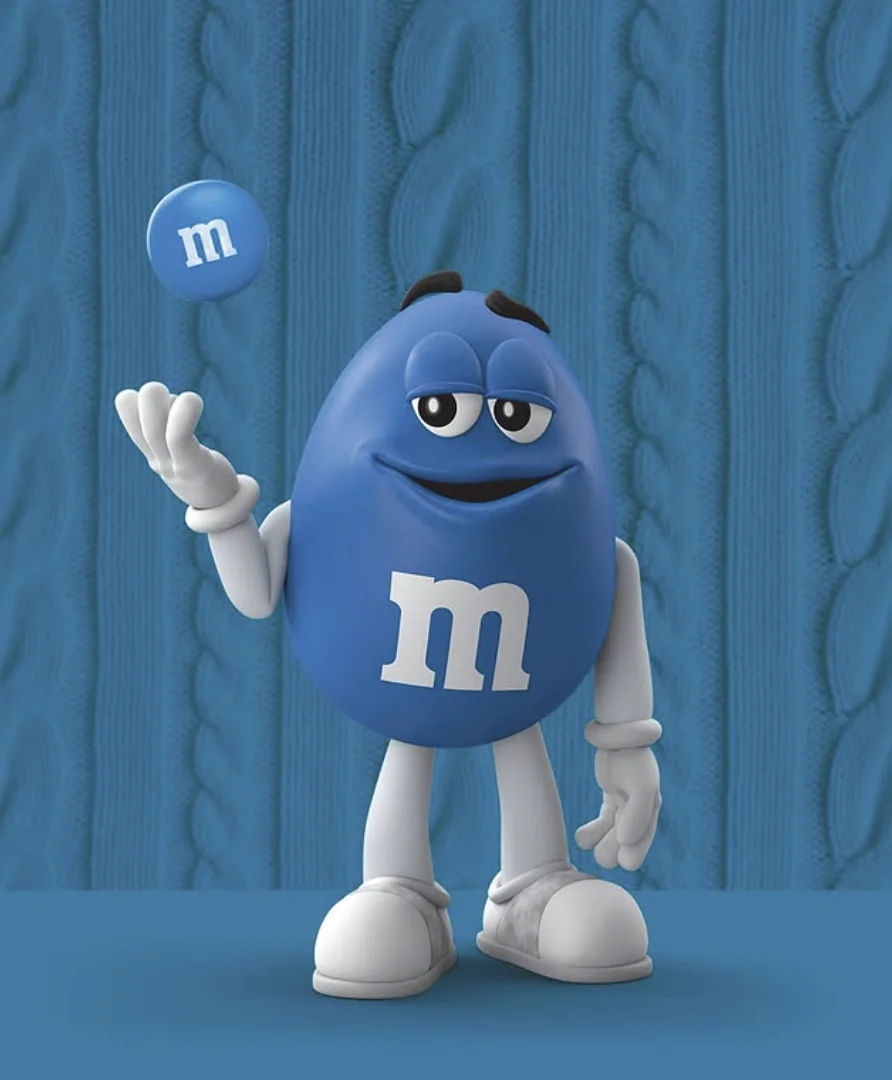 O personagem M&M Azul em pé, sorrindo e equilibrando um confeito azul no ar com uma das mãos. O fundo é uma textura de suéter de tricô azul-cerúleo.