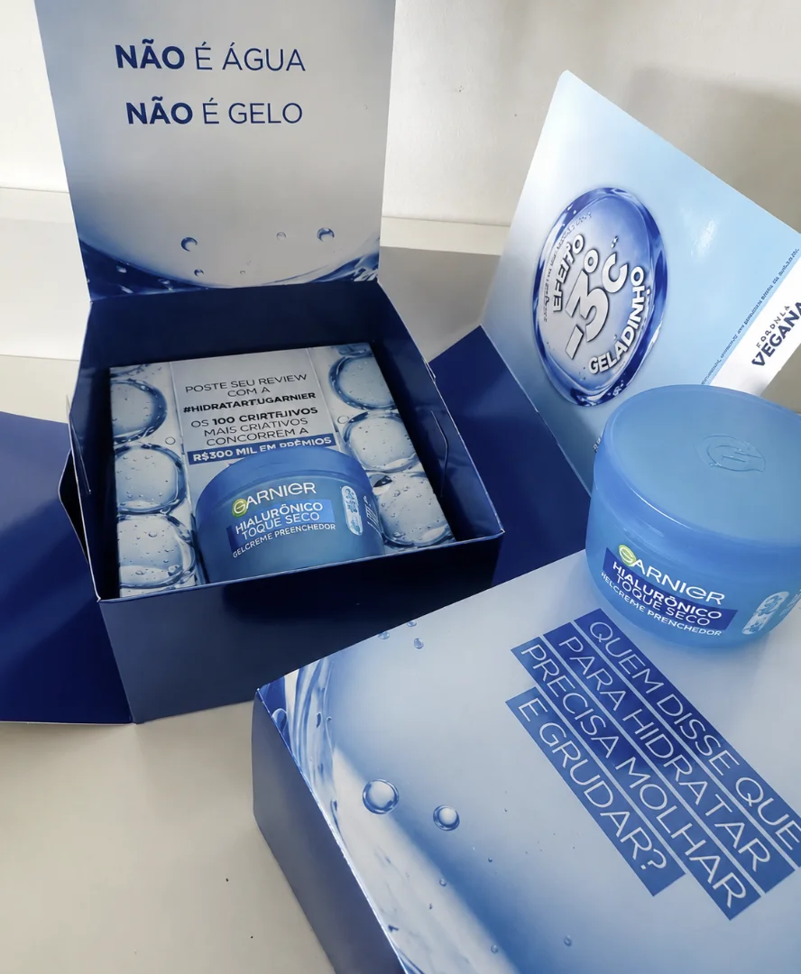 Kit promocional aberto da Garnier contendo o gel-creme Hialurônico Toque Seco e materiais informativos com estética de água e gelo.