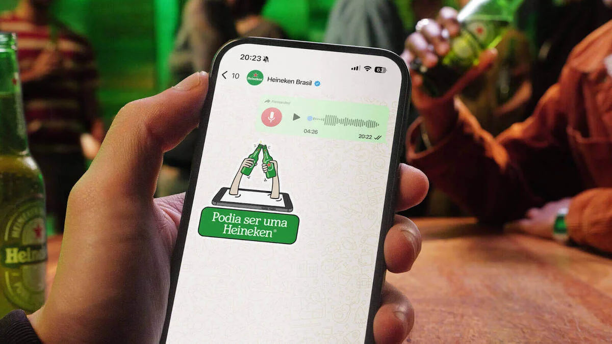 Celular exibindo campanha “Podia ser uma Heineken” com áudio longo no WhatsApp enquanto pessoas bebem cerveja em um bar.