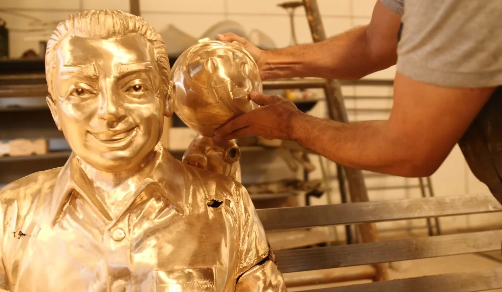 Banco de bronze em homenagem a Mauricio de Sousa é montado com escultura dourada e personagem ao fundo.