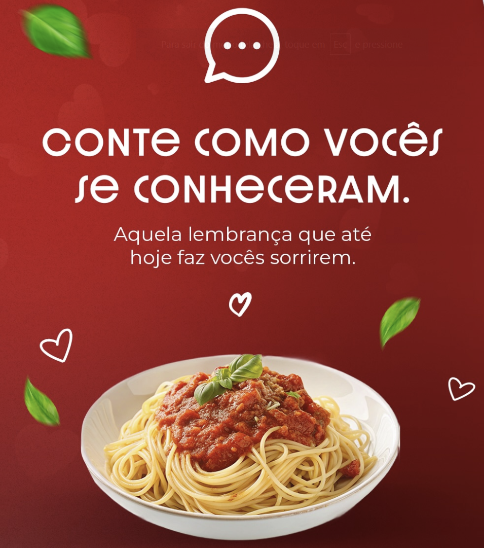 Imagem promocional da Olé Alimentos com fundo vermelho. No topo, um ícone de balão de fala com reticências. O texto em branco e em negrito lê: "CONTE COMO VOCÊS SE CONHECERAM." Abaixo, um texto menor diz: "Aquela lembrança que até hoje faz vocês sorrirem." A parte inferior mostra uma tigela de espaguete com molho de tomate e manjericão, cercada por pequenos corações brancos e folhas de manjericão flutuantes.