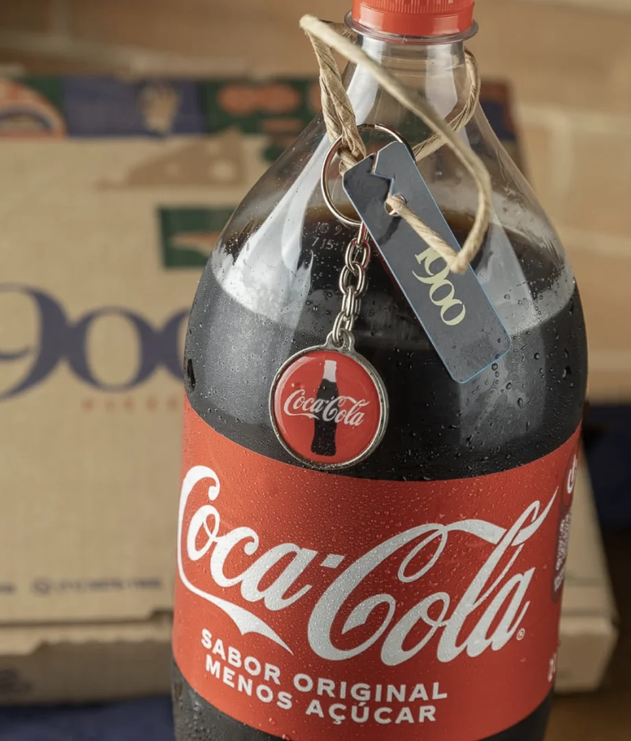 Garrafa de Coca-Cola com chaveiro colecionável temático da marca e caixa da 1900 Pizzeria ao fundo.