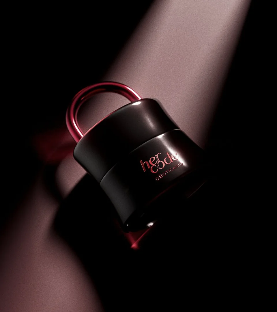Perfume Her Code de O Boticário com embalagem preta e detalhe vermelho metálico em fundo escuro iluminado.