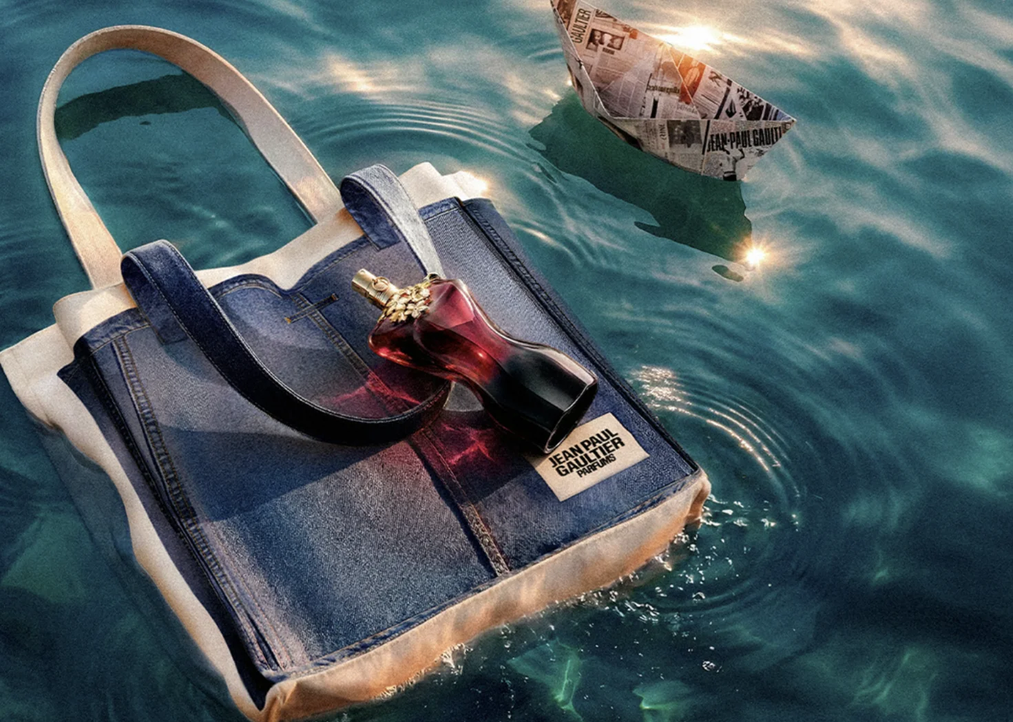 Perfume Jean Paul Gaultier sobre bolsa jeans flutuando na água.