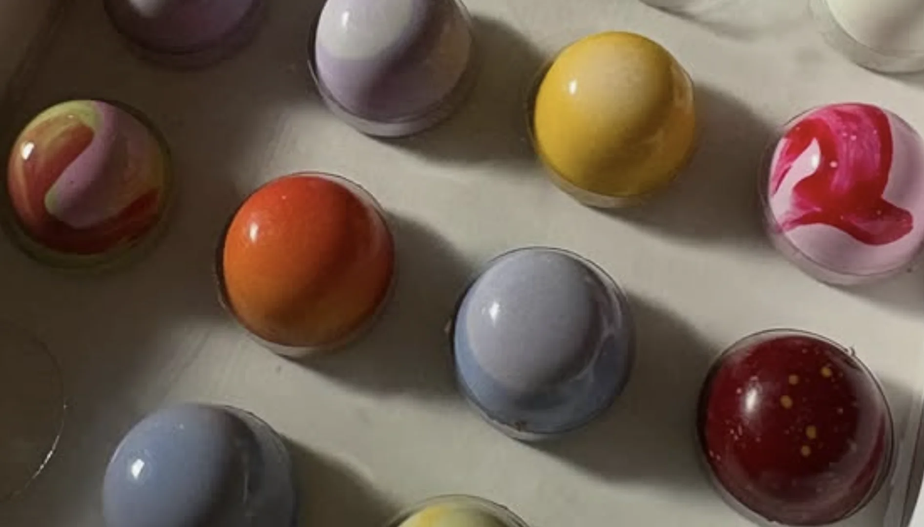 Caixa com bombons artesanais coloridos e brilhantes, em diferentes sabores, organizados em fileiras.