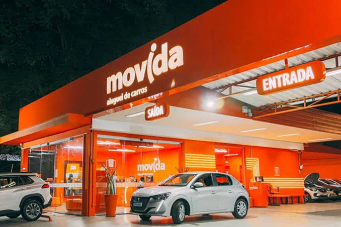 Fachada iluminada de uma unidade da Movida aluguel de carros durante a noite.