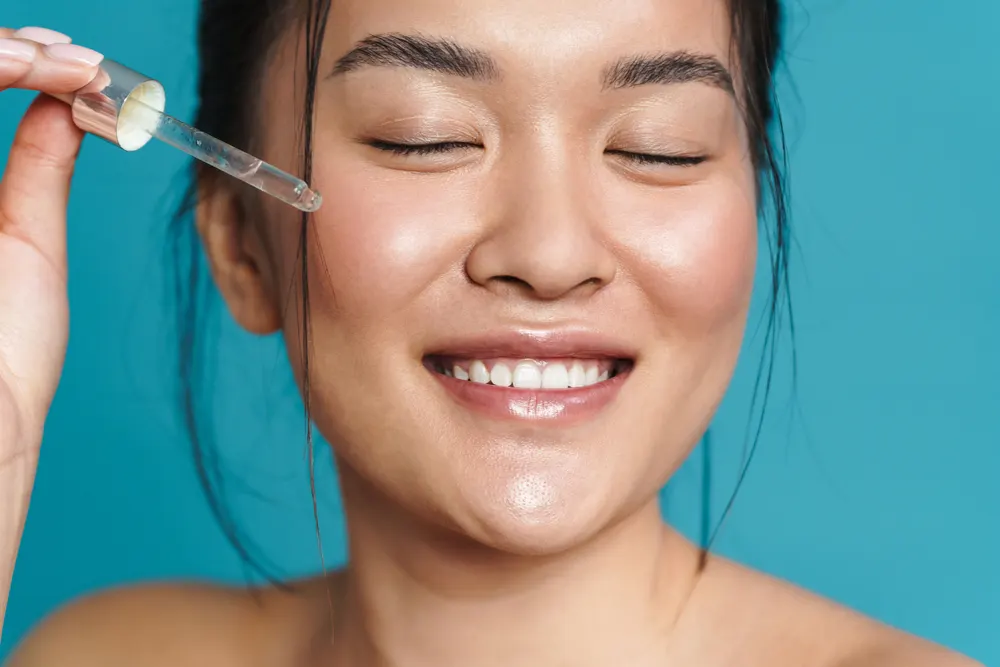 Mulher aplicando sérum facial com conta-gotas em rotina de skincare iluminada.