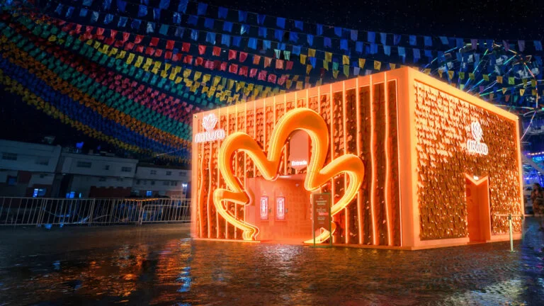 Espaço iluminado da Natura em festa de São João com bandeirinhas coloridas e estrutura temática laranja.