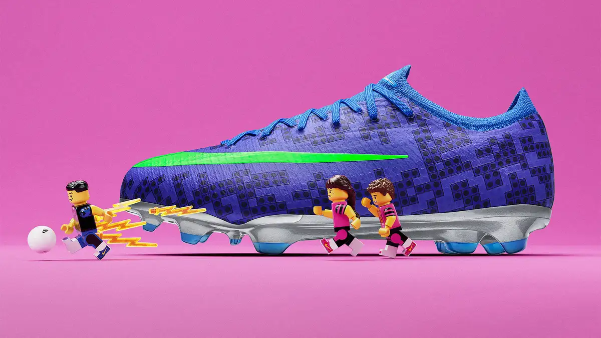 Chuteira azul e roxa da Nike com textura inspirada em LEGO aparece acompanhada de mini personagens jogando futebol.