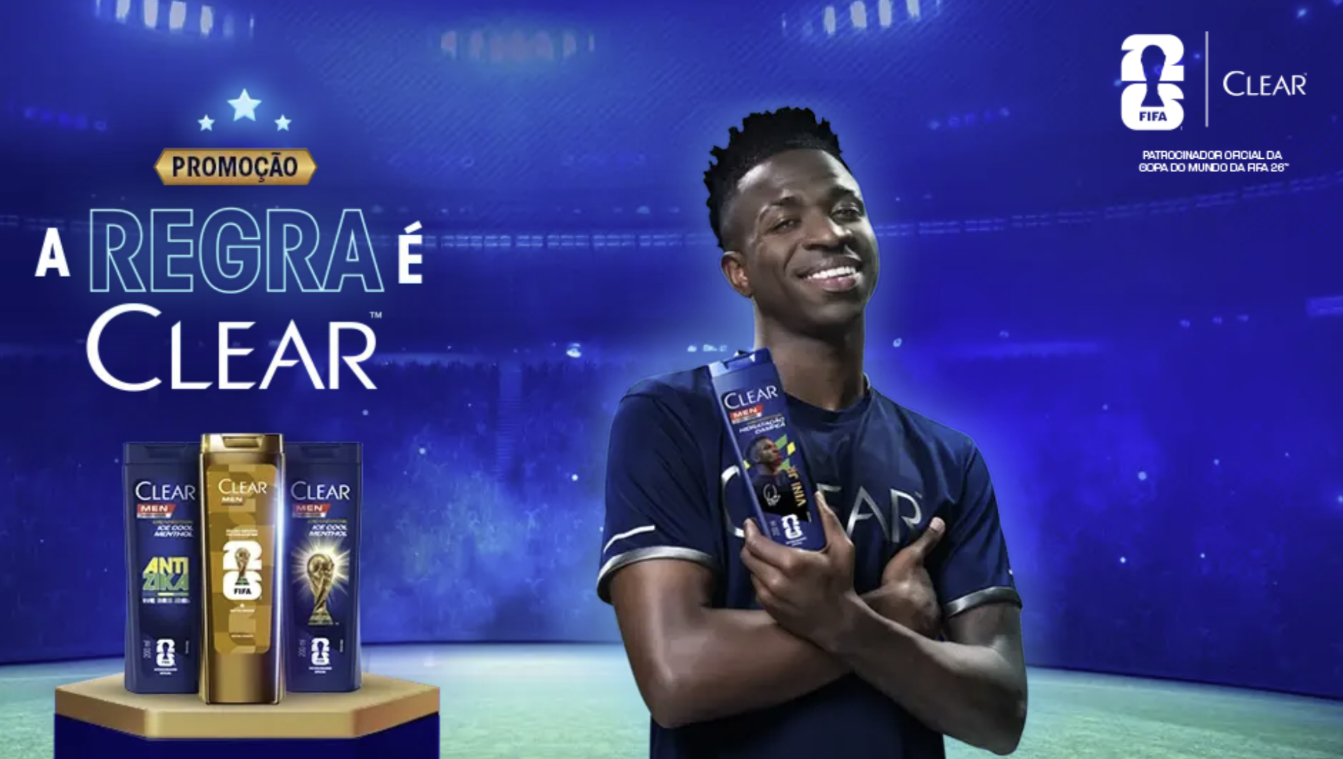 Banner promocional da campanha "A Regra é Clear" com o jogador Vini Jr. sorrindo ao centro, de braços cruzados e segurando um shampoo Clear Men. À esquerda, três frascos de shampoo estão expostos em um totem, e ao fundo há um estádio de futebol sob luzes azuis.