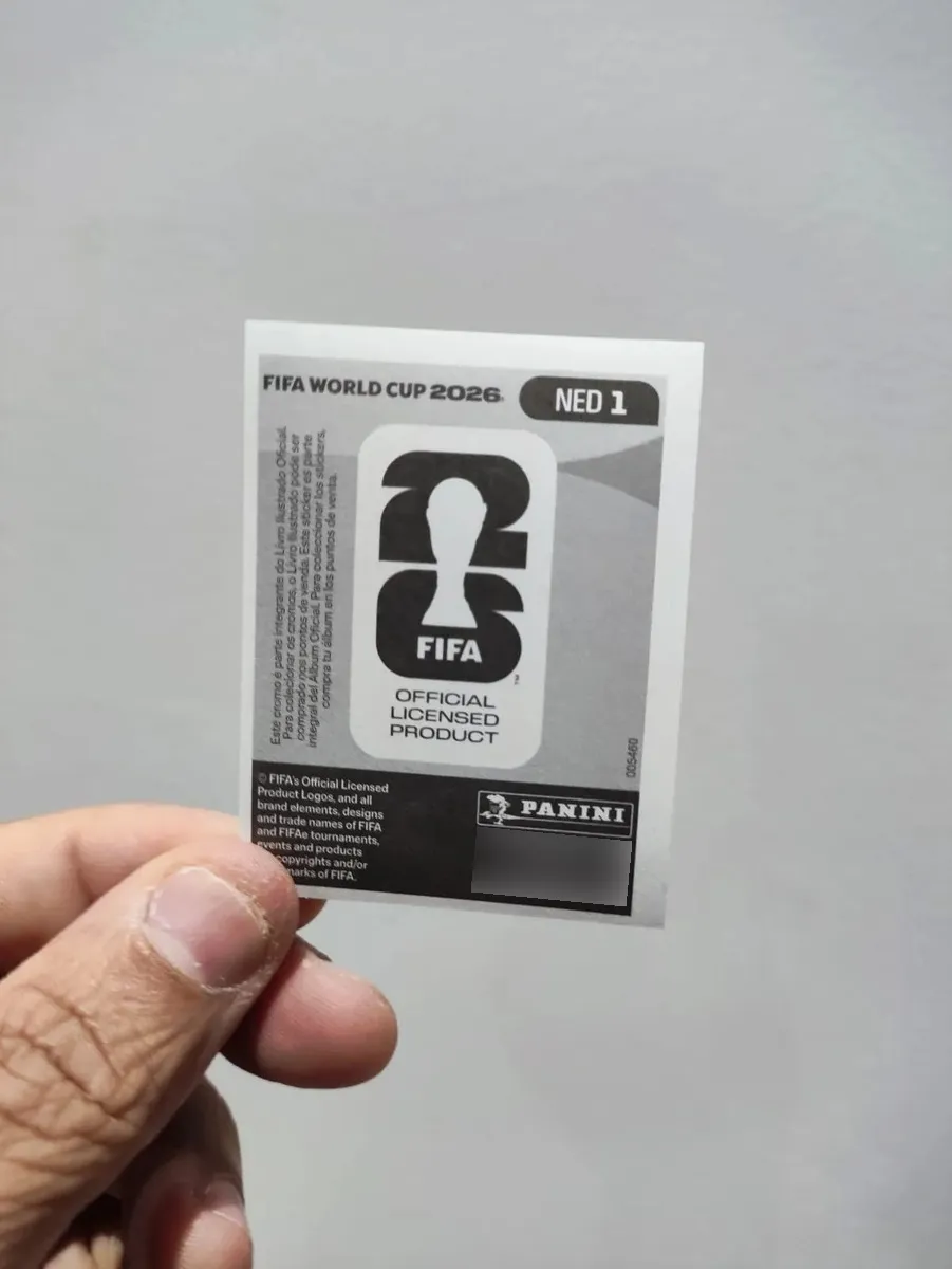 Pessoa segurando o verso de uma figurinha oficial da Copa do Mundo 2026 com fundo neutro.