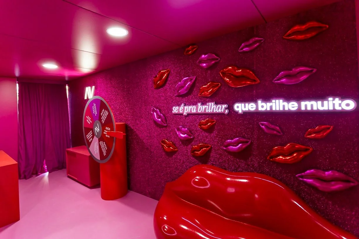 Área instagramável da Avon com sofá em formato de boca, painel de lábios e roda de brindes.