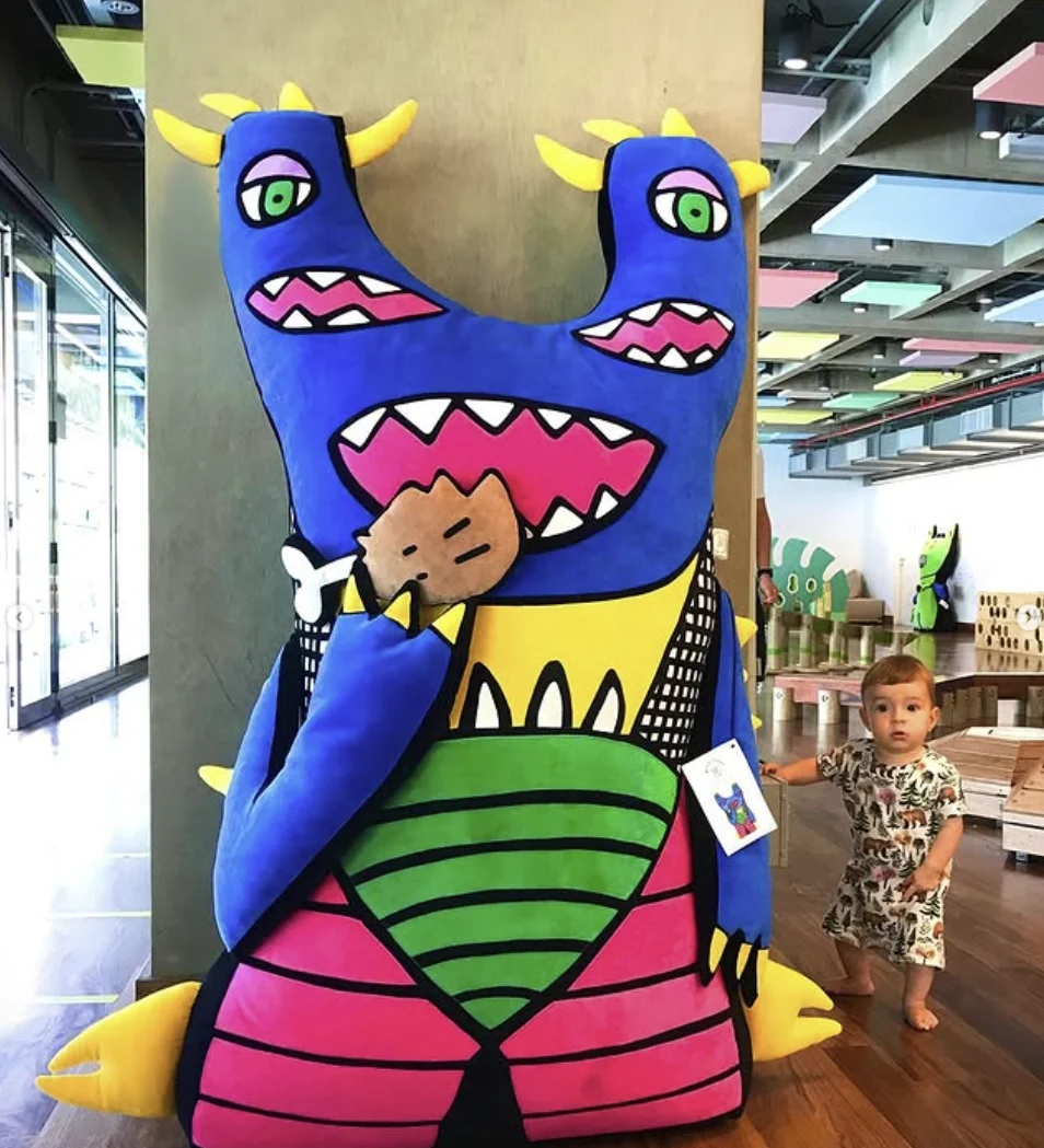 Bebê observa boneco gigante azul e colorido criado a partir de desenho infantil em espaço da TinTinTins.