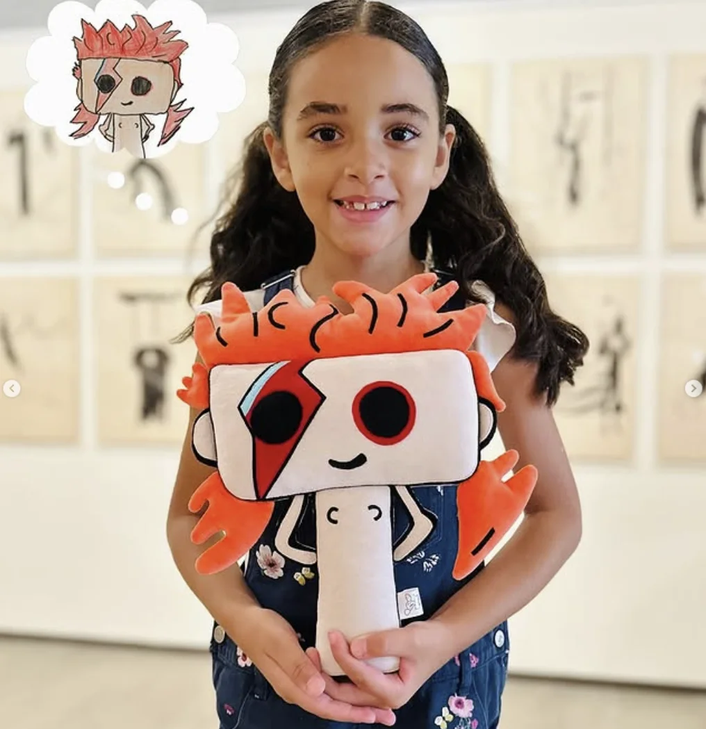 Menina segura boneco de pelúcia criado a partir de desenho infantil com inspiração em personagem colorido.