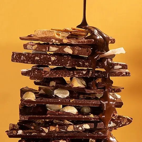Barra de chocolate artesanal empilhada com castanhas e cobertura de chocolate derretido.