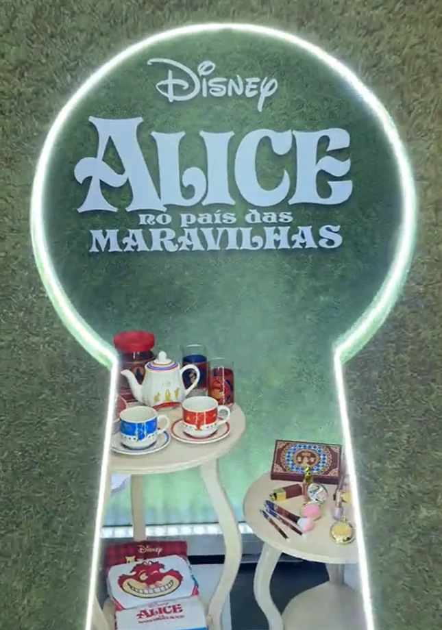 Espaço temático de Alice no País das Maravilhas com logotipo da Disney, mesa decorada com xícaras, bule, cosméticos e itens da coleção da Avon.