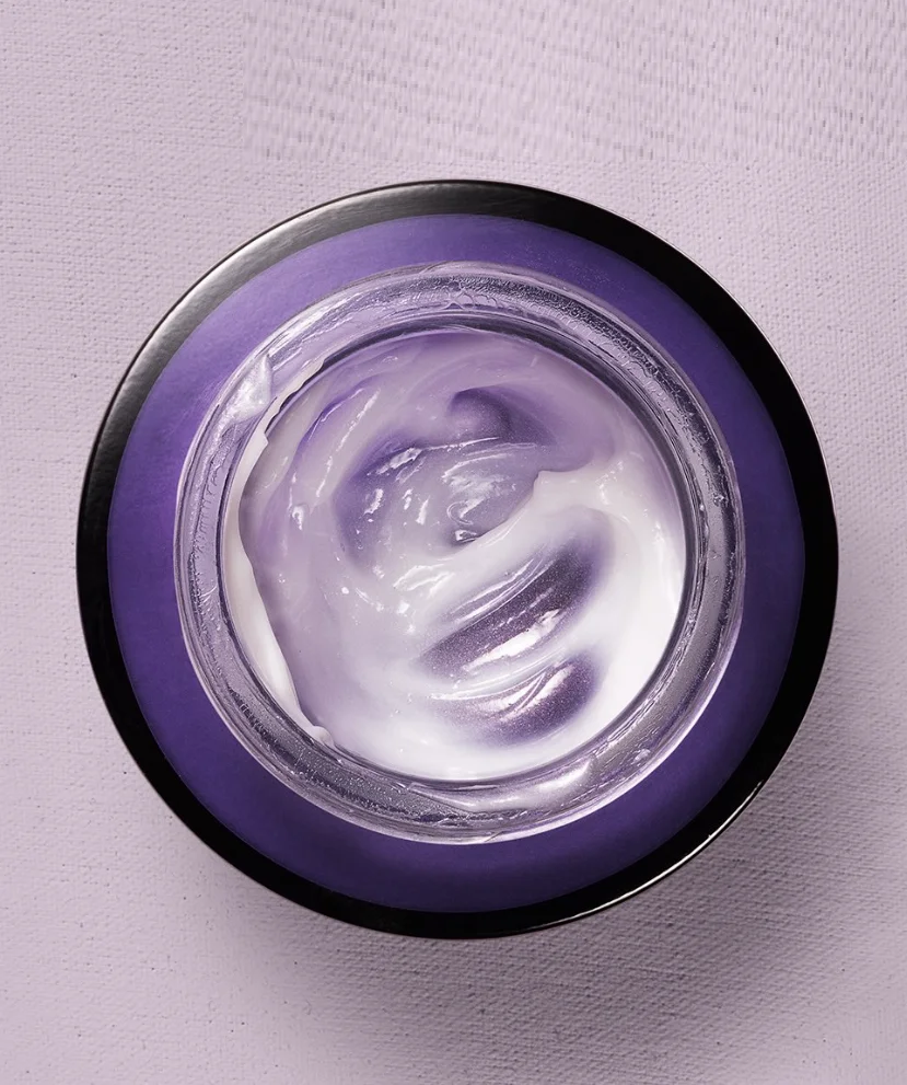 Pote de creme Avon aberto com produto já utilizado em destaque sobre fundo lilás.
