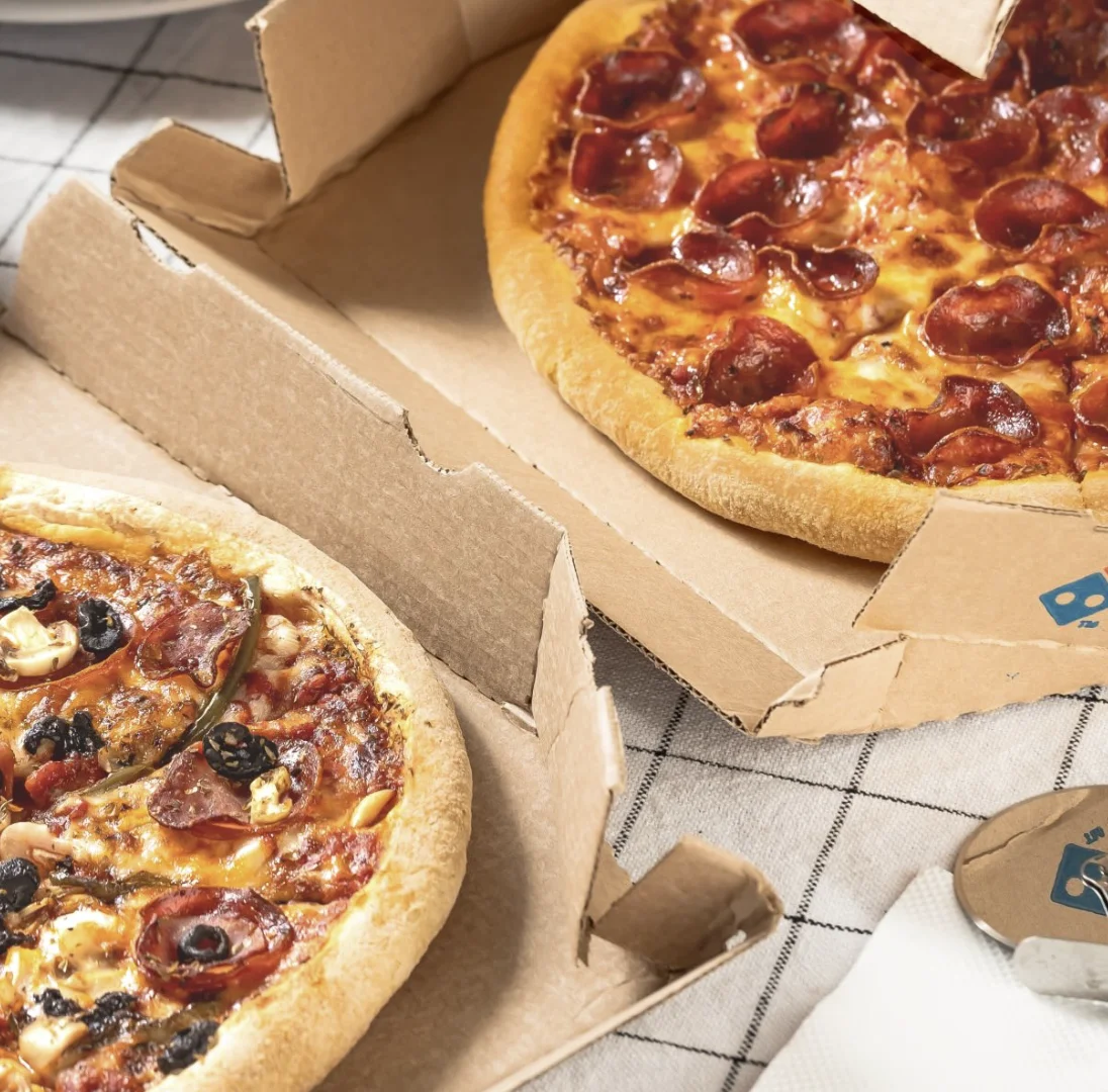Arte da Domino's Pizza mostra celular com o aplicativo aberto ao lado de um card de "Amigos Próximos" do Instagram sobre fundo com pizza desfocada