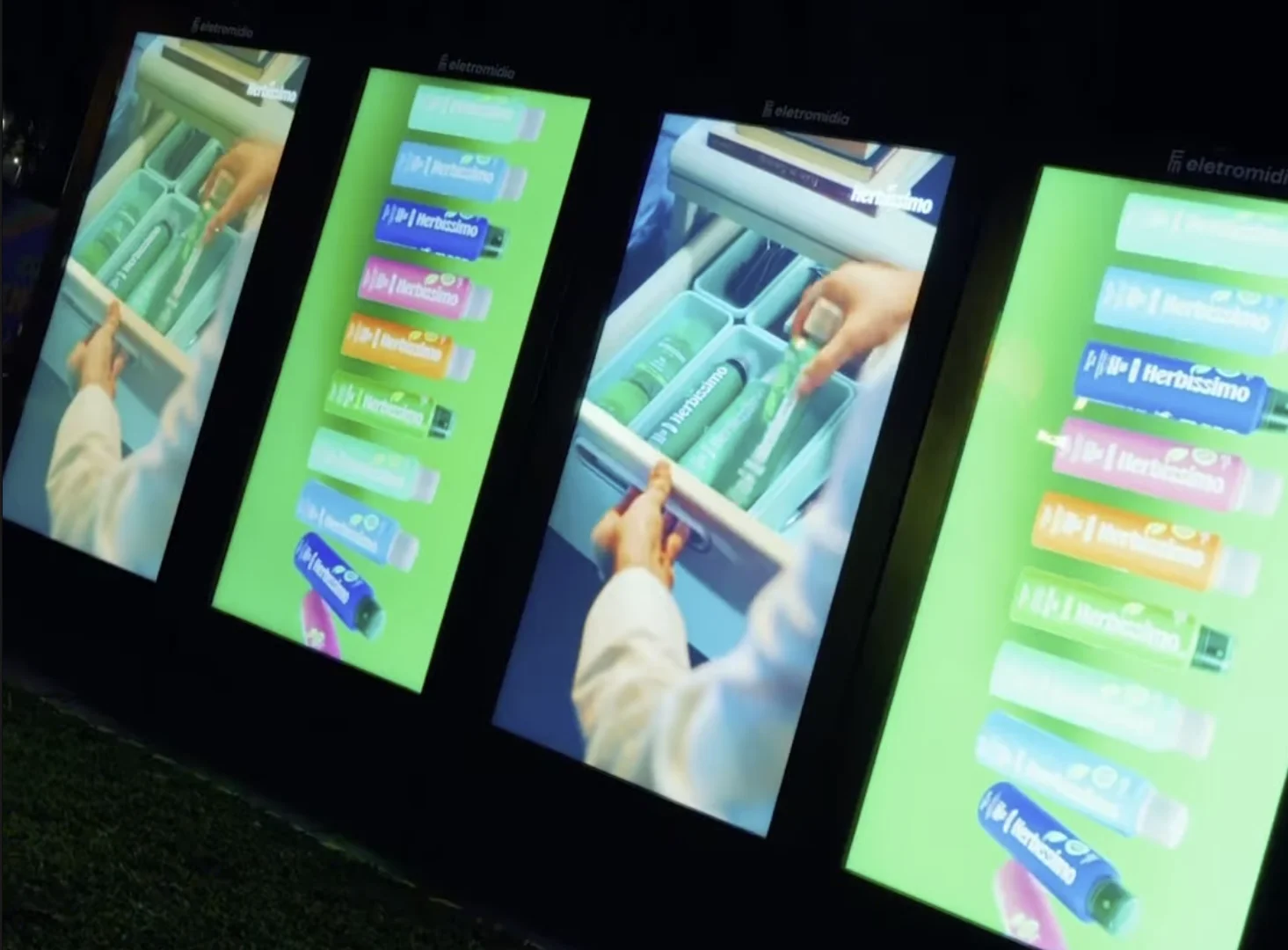 Painéis digitais da Herbíssimo exibem o novo aerossol zero alumínio durante ativação na Arena Brasileira.