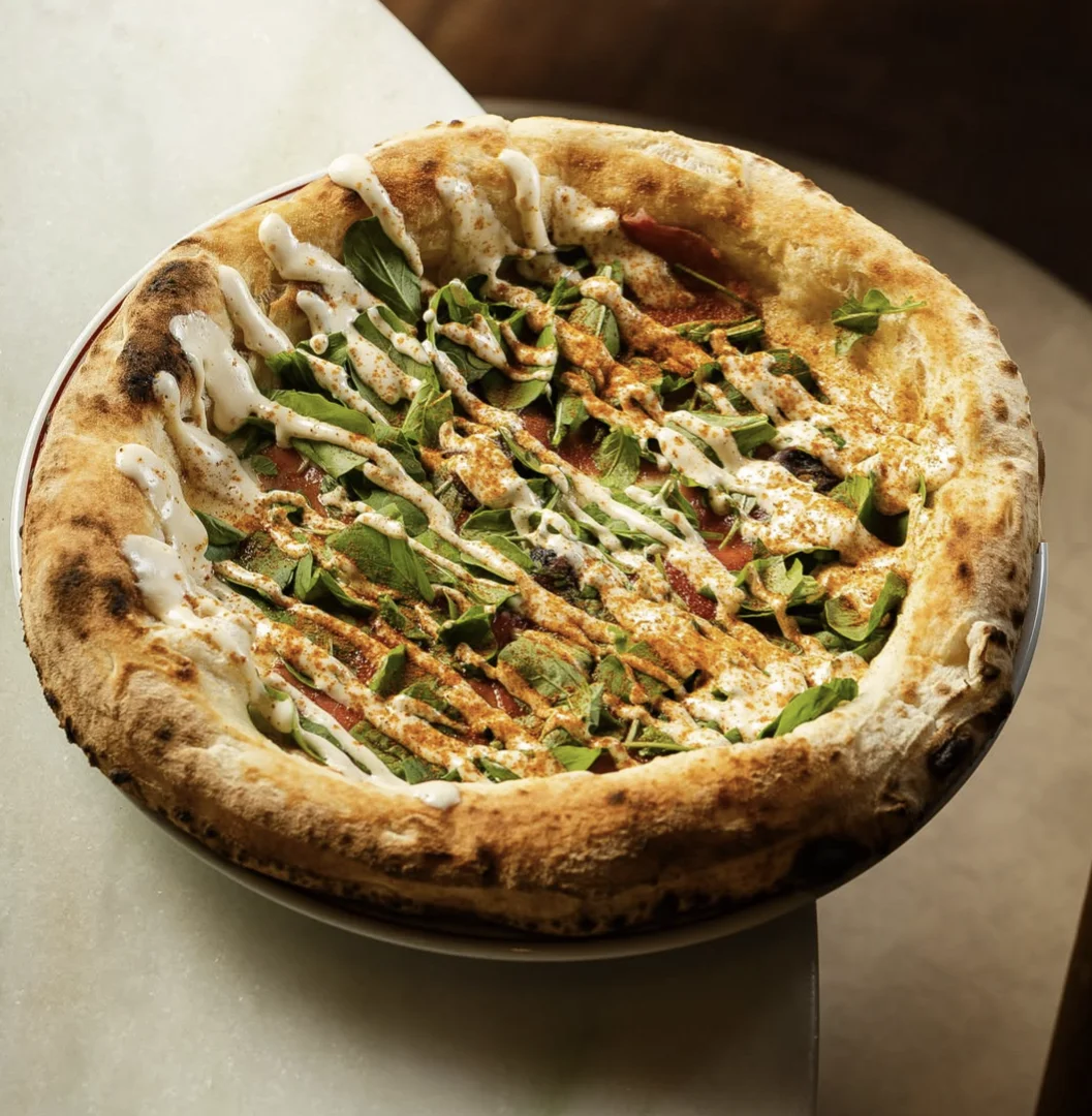 Pizza napolitana da La Braciera com massa artesanal alta, folhas verdes e molho cremoso por cima.