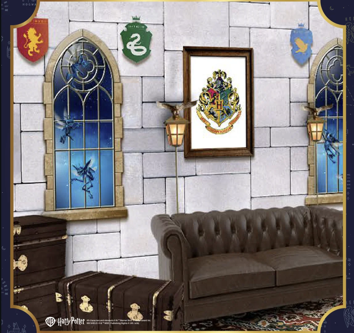 Cenário inspirado em Hogwarts com sofá, malas, brasão da escola e janelas temáticas de Harry Potter.