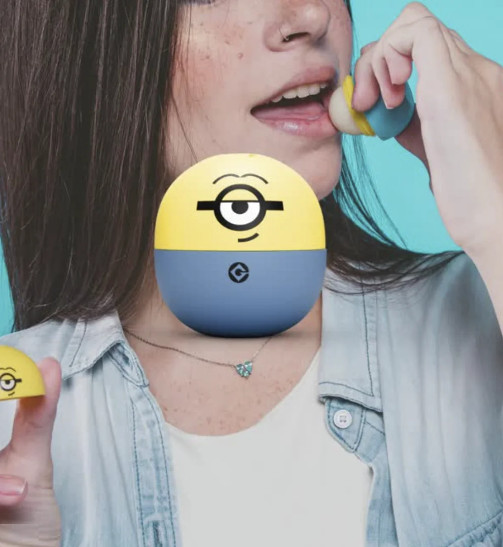 Pessoa aplicando hidratante labial da Beta inspirado nos Minions com embalagem amarela e azul em formato colecionável.