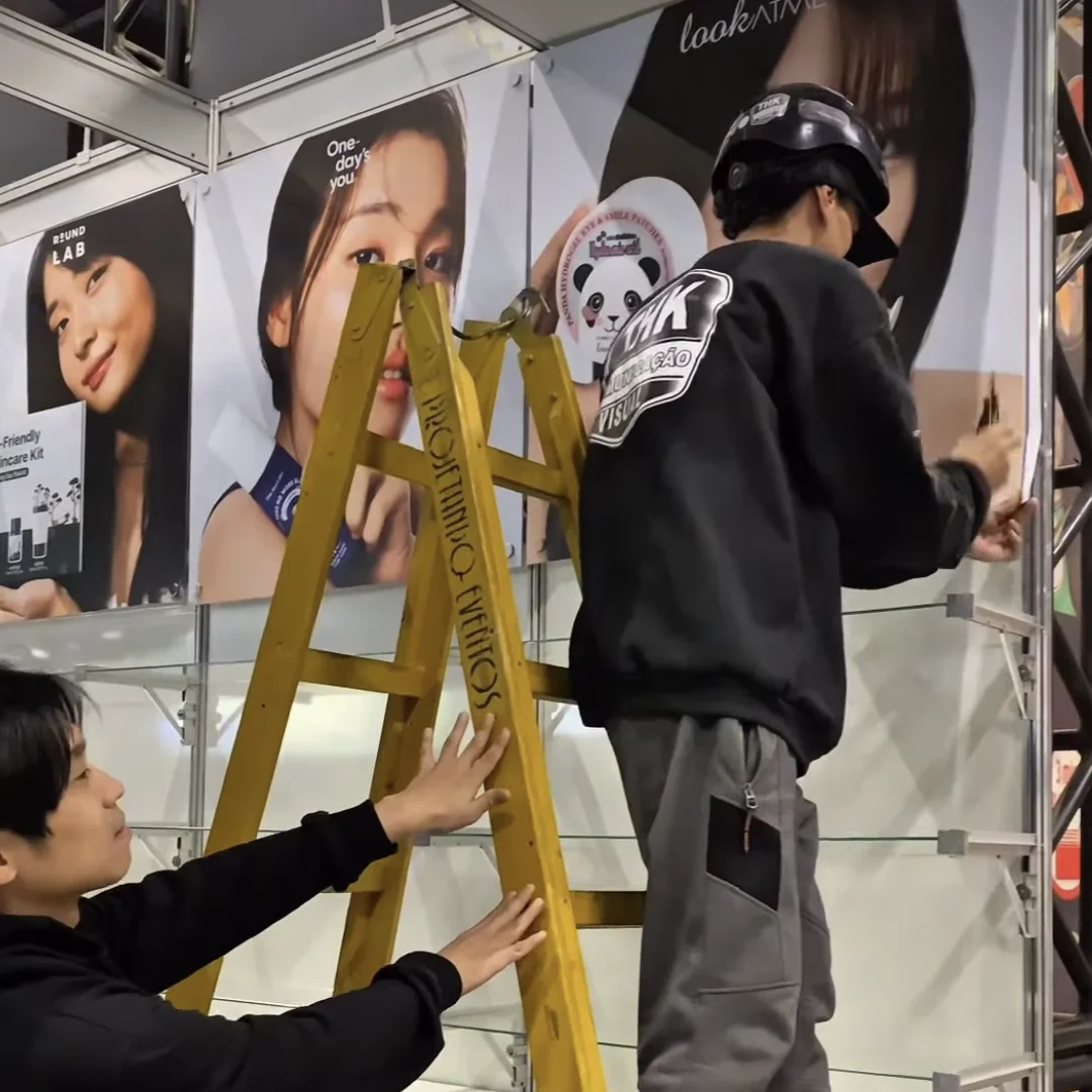 Equipe monta o estande da KS Cosméticos com painéis de marcas coreanas de skincare antes da abertura do evento.