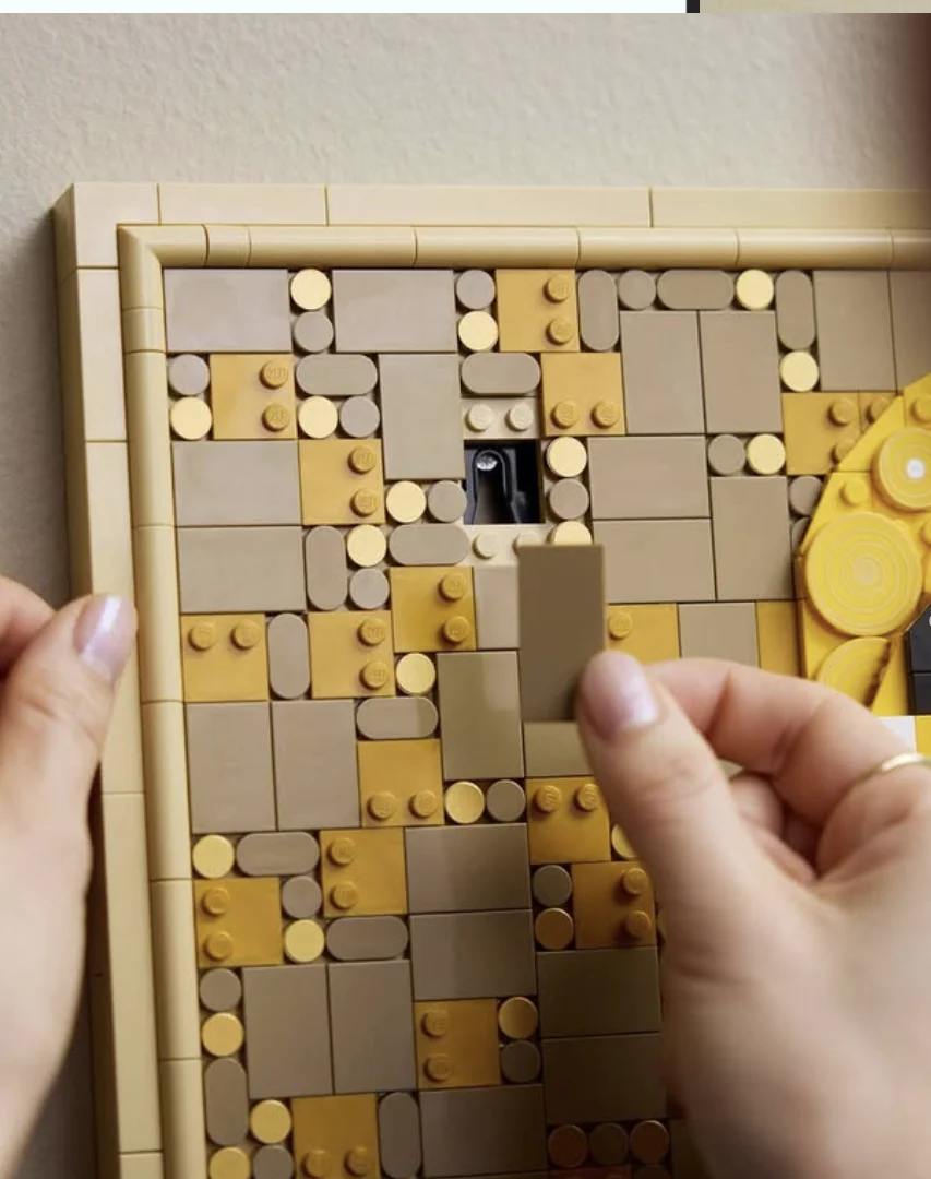 Pessoa encaixando peças na moldura do conjunto LEGO Art "O Beijo", mostrando detalhes da montagem e do acabamento.Processo de montagem evidencia os detalhes do quadro da LEGO.